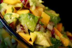 A close up view of a bowl of chunky mango salsa. Mango, avocado, red onion, and cilantro are all visible.