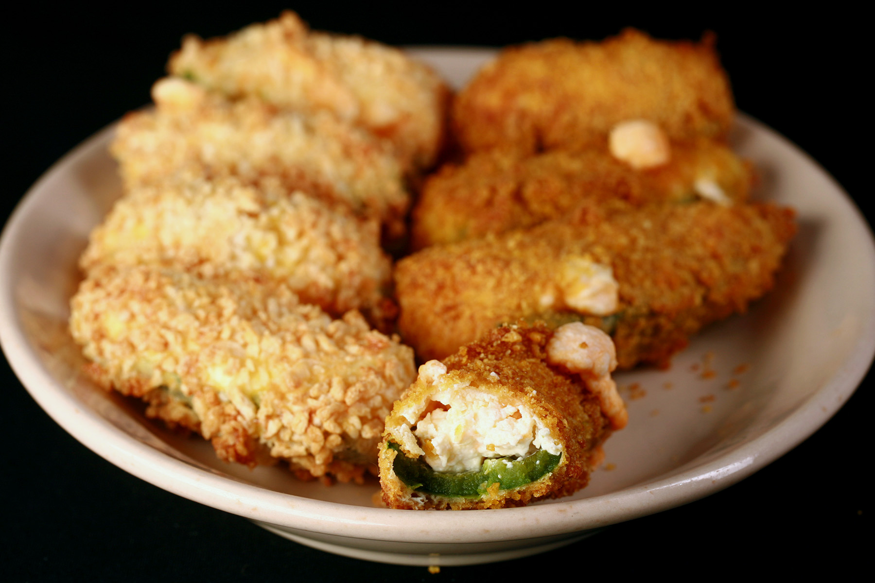 A close up view of air fryer gluten-free jalapeno poppers. One has a bite taken out of it.