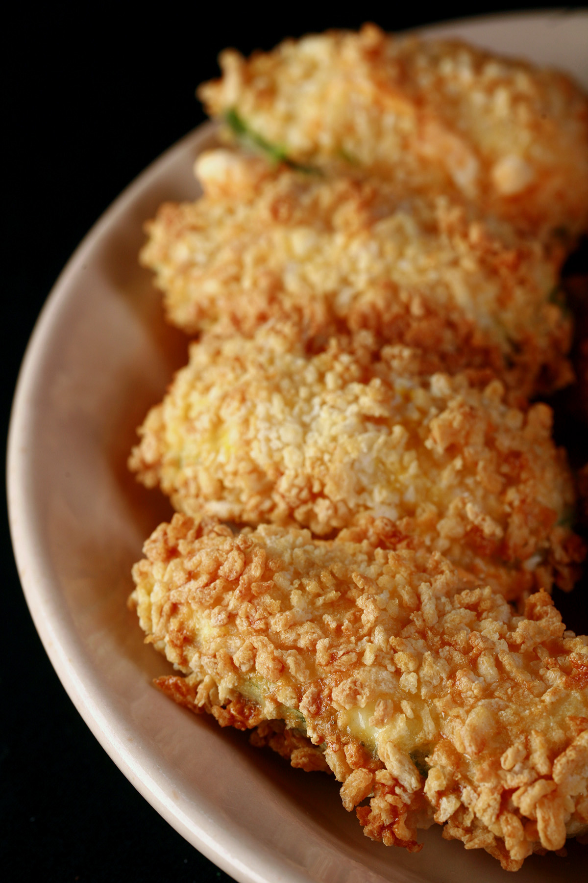 Air fried gluten free jalapeno poppers on a small ivory plate. These 4 are coated in gluten-free panko crumbs.