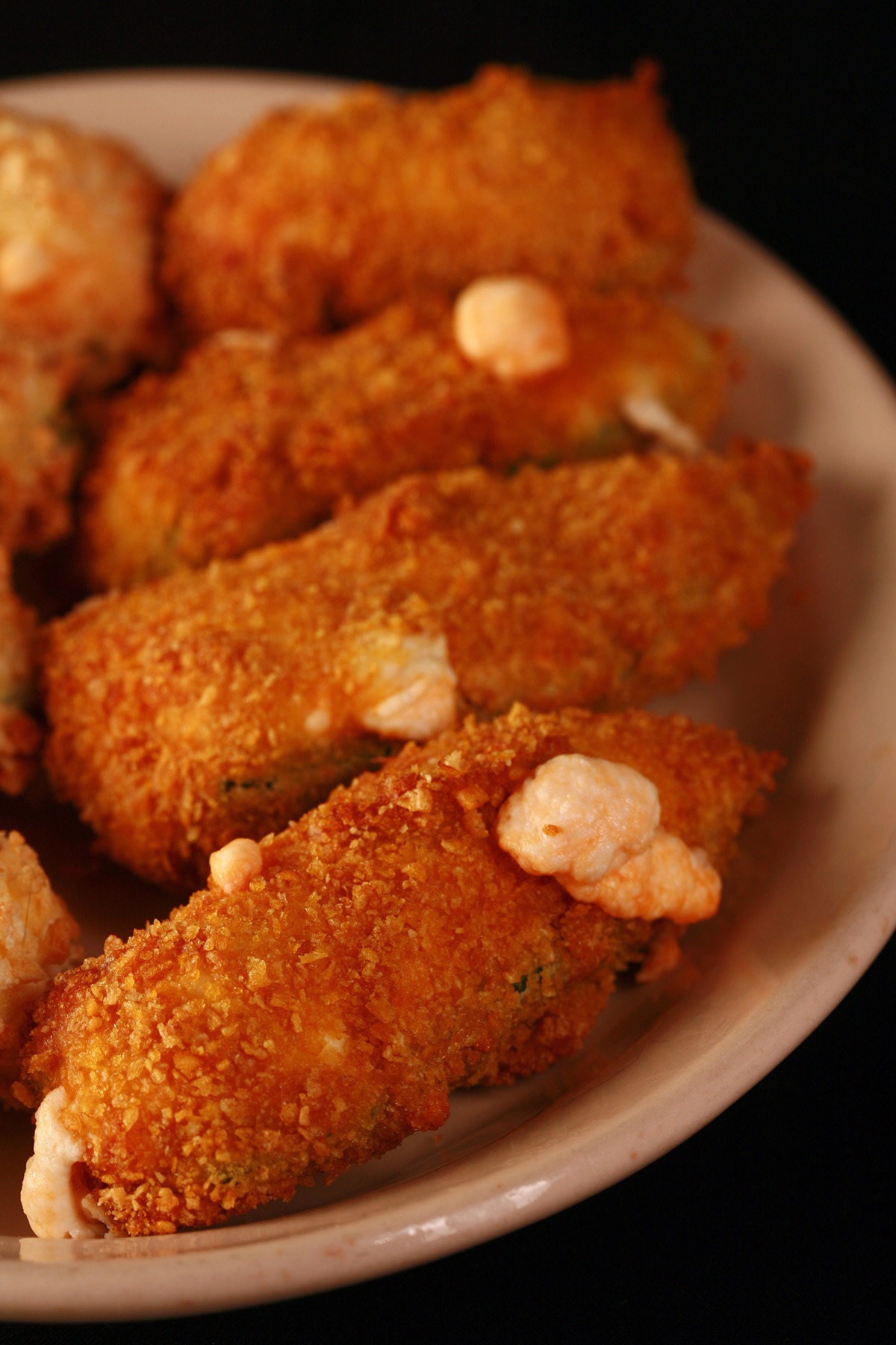 Air fried gluten free jalapeno poppers on a small ivory plate. These 4 are coated in corn flake crumbs.