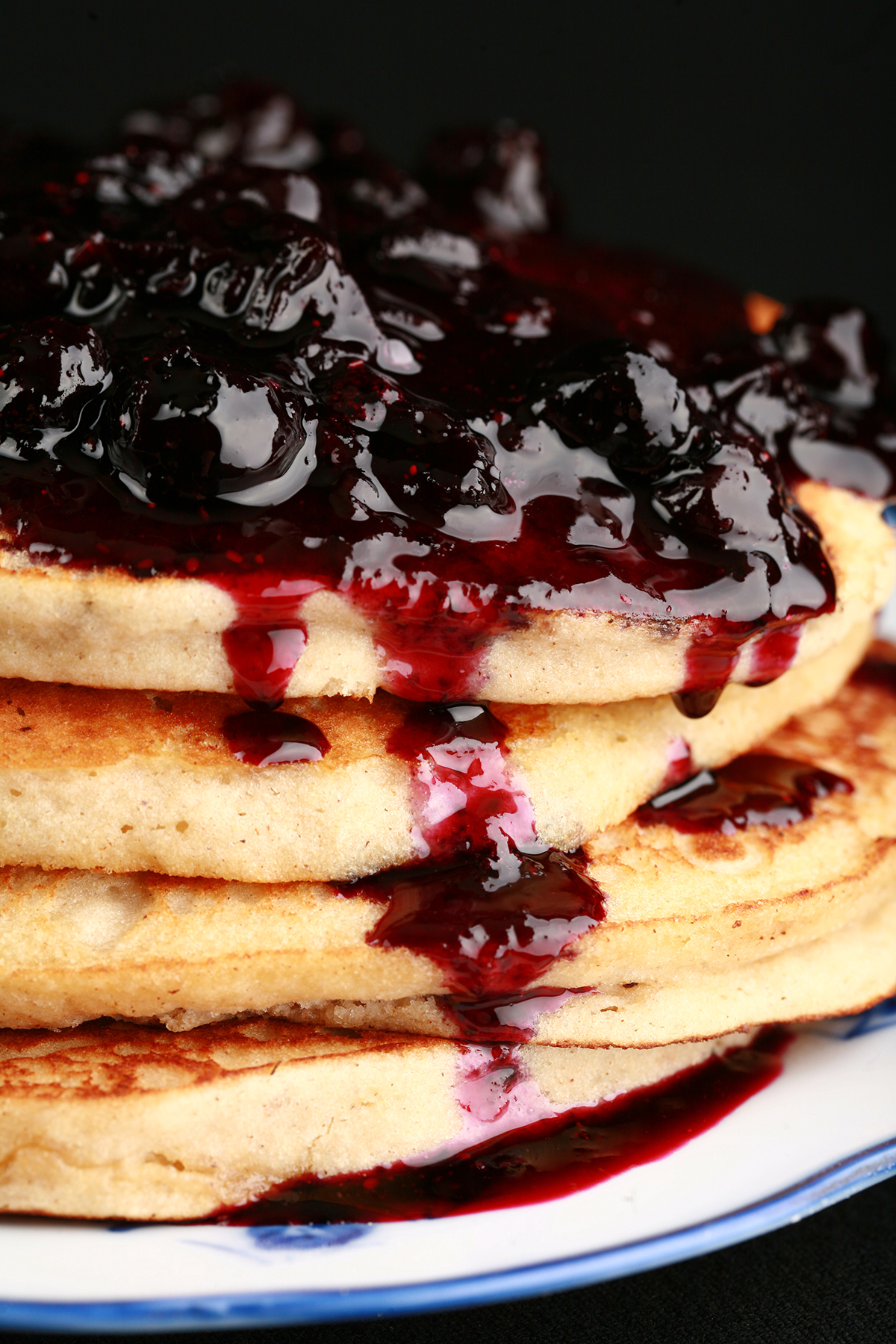 A stack of gluten-free banana buckwheat pancakes on a plate. It is topped with fresh blueberry sauce.
