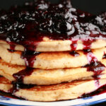 A stack of gluten-free banana buckwheat pancakes on a plate. It is topped with fresh blueberry sauce.