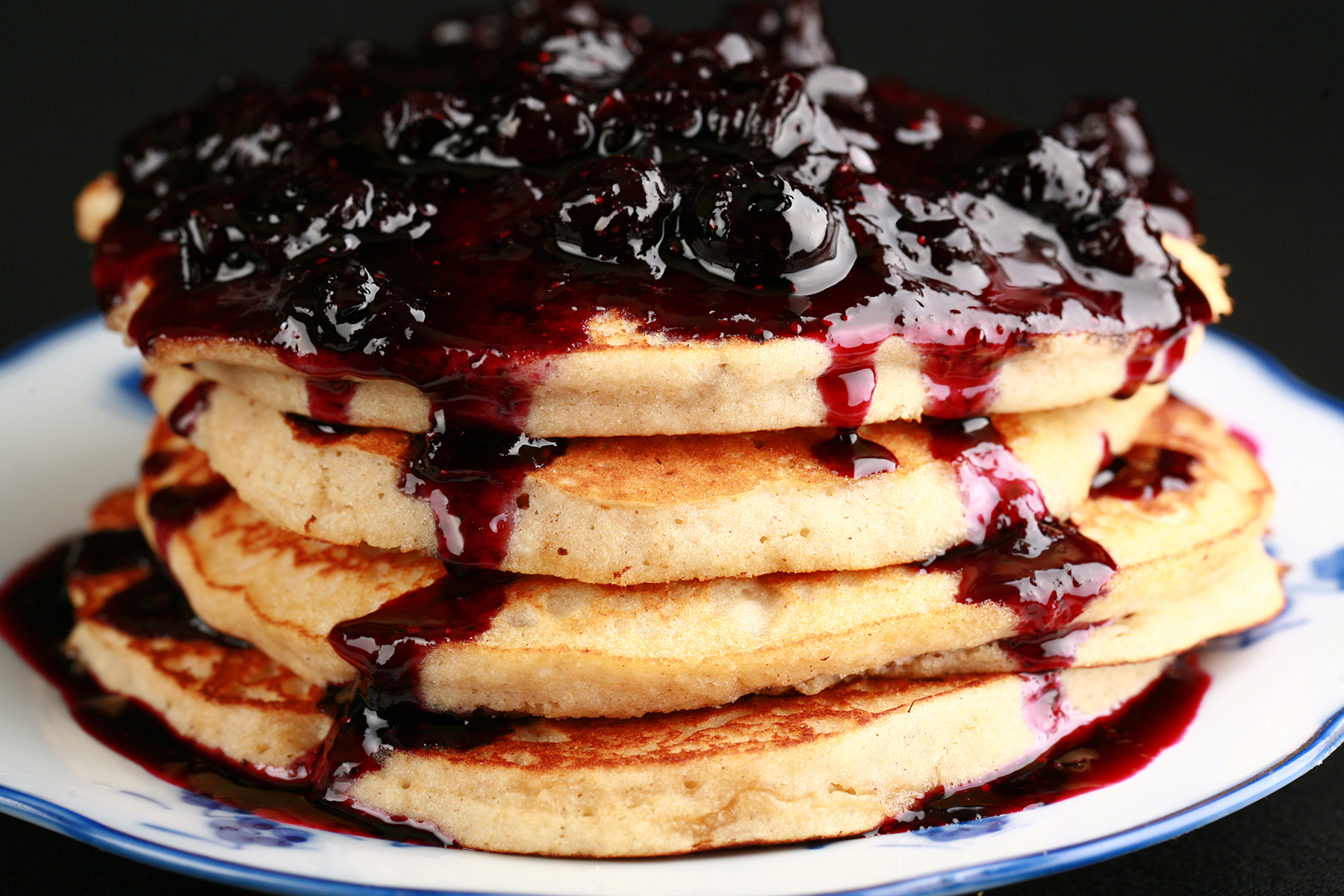 A stack of gluten-free banana buckwheat pancakes on a plate. It is topped with fresh blueberry sauce.