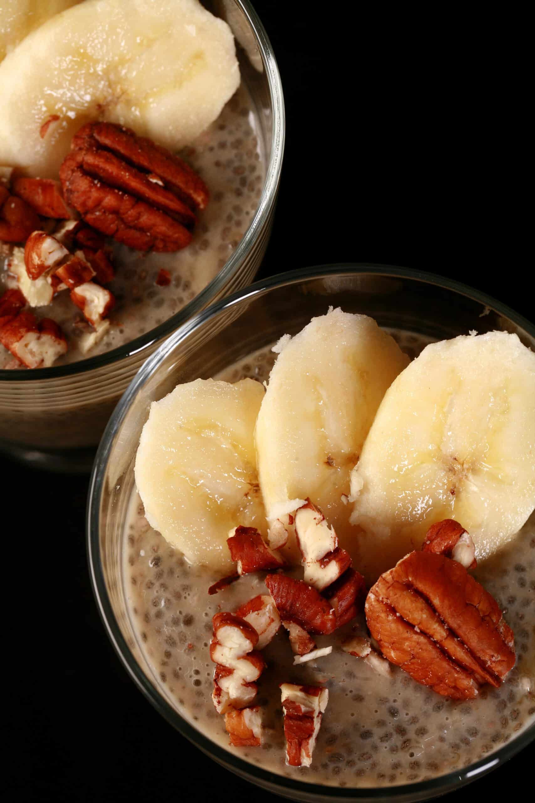 2 serving glasses of banana chia pudding, topped with banana slices and pecans.