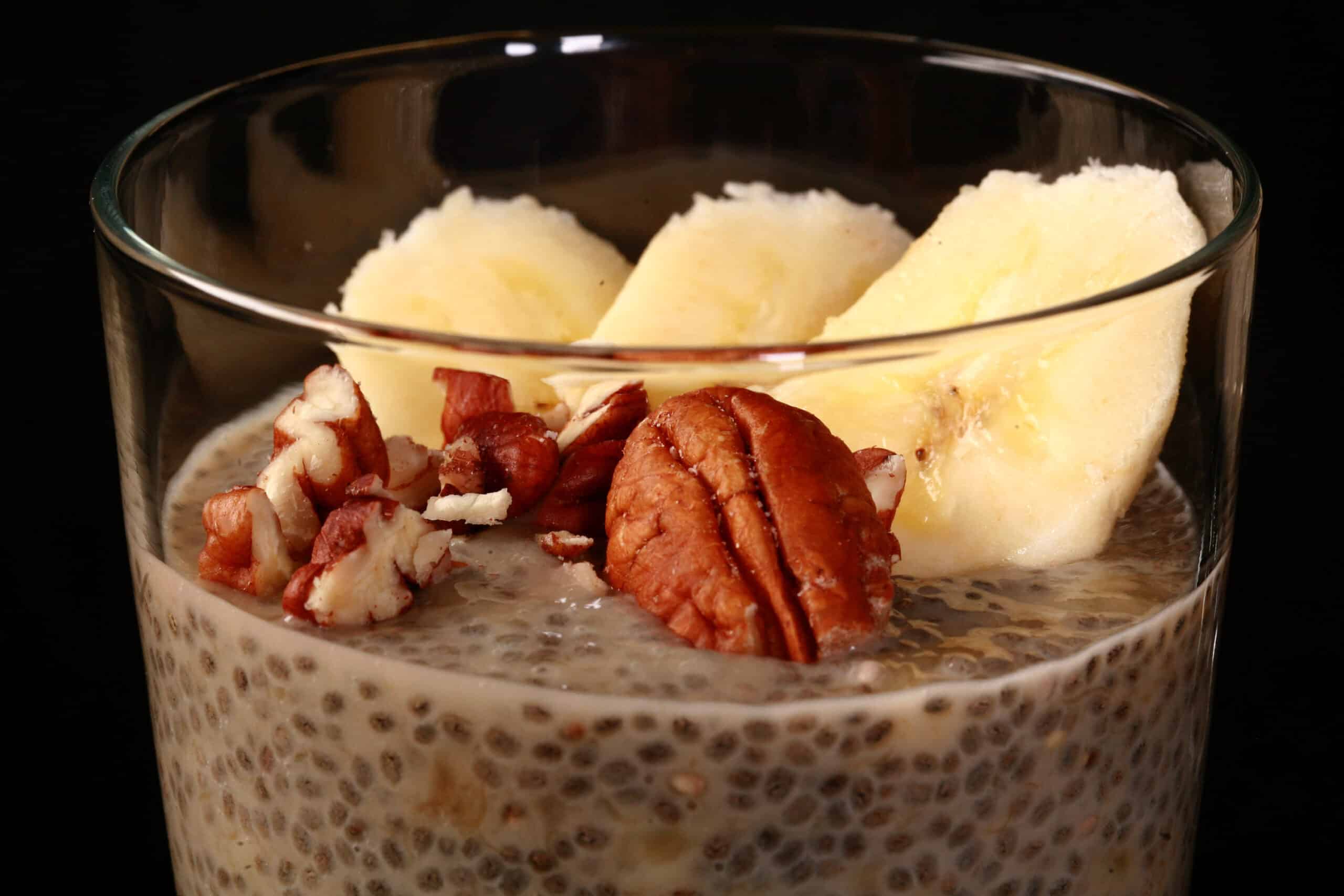 A close up view of a glass of banana chia pudding, topped with banana slices and pecans.
