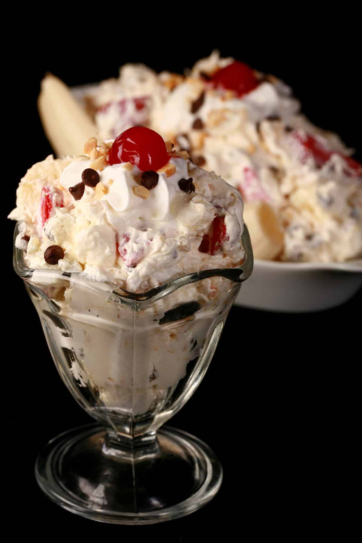 Banana Split Fluff Salad in a glass bowl, in front of a serving done up like an actual banana split.