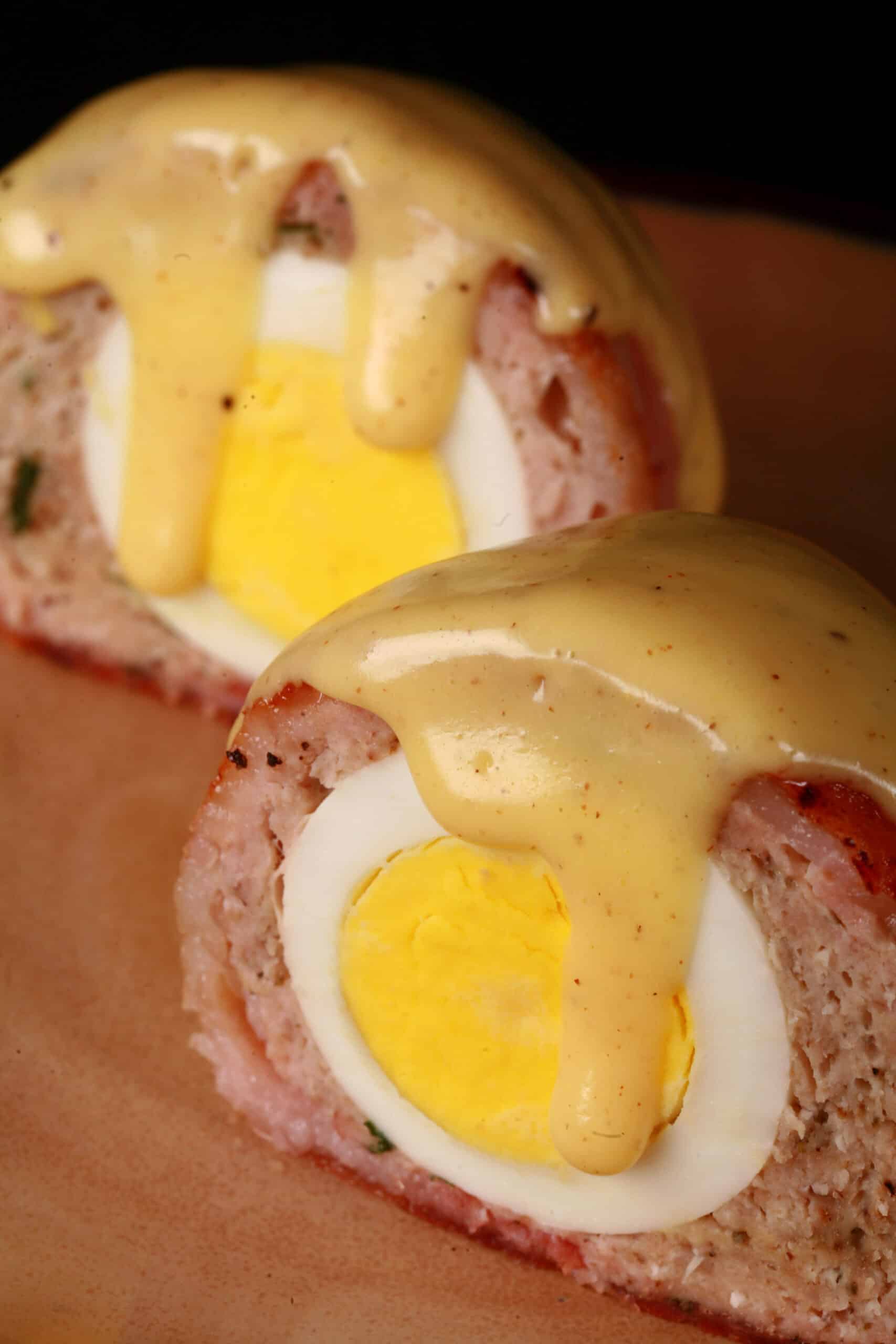 A hardboiled-egg stuffed meatloaf cut in half. Itโs wrapped in bacon and topped with Hollandaise sauce.
