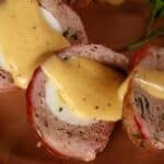 A sliced individual breakfast meatloaf, wrapped in bacon, stuffed with a hard boiled egg, and topped with hollandaise sauce.