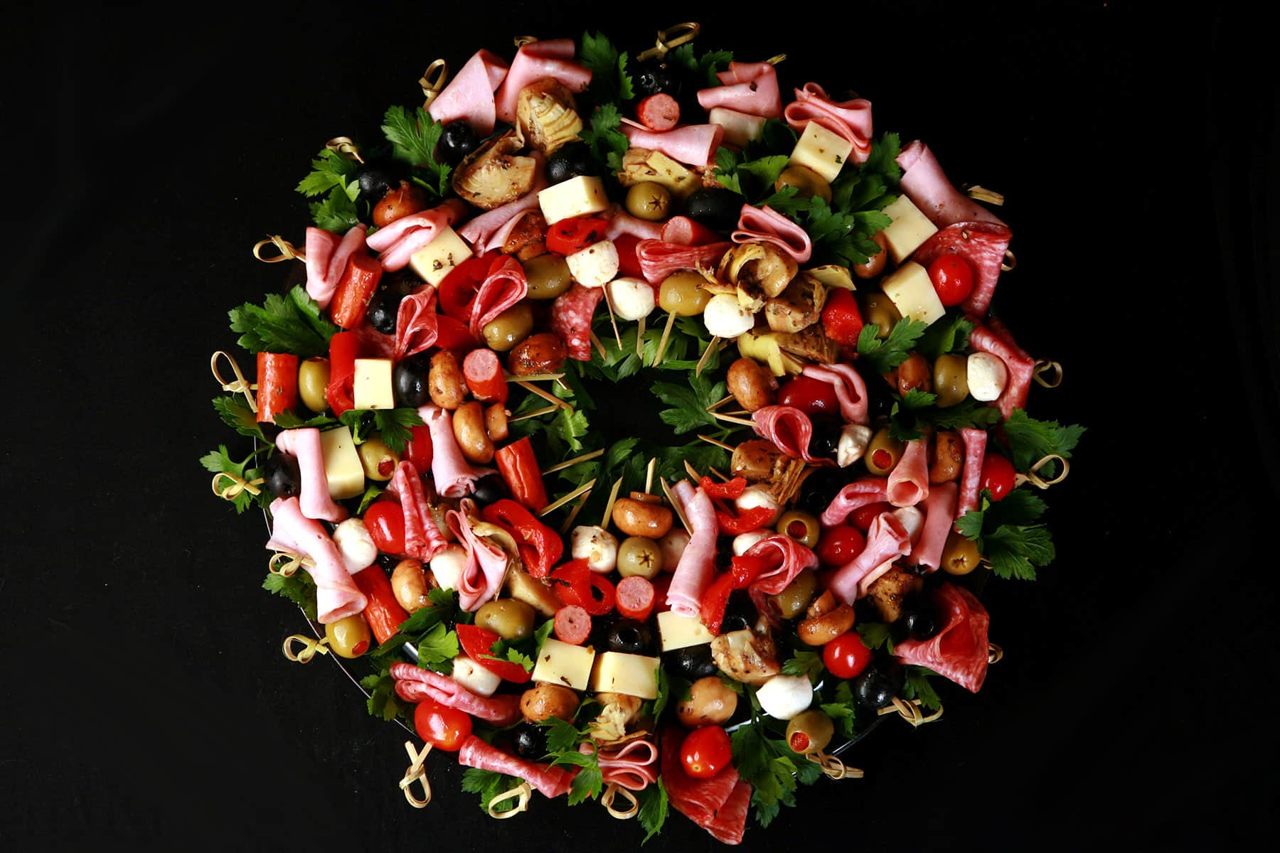 A wreath shaped charcuterie board, made up of antipasto skewers featuring various meats, cheeses, and olives.