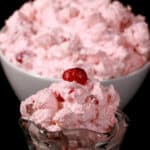 A serving glass of cherry fluff salad, in front of a bowl of it.