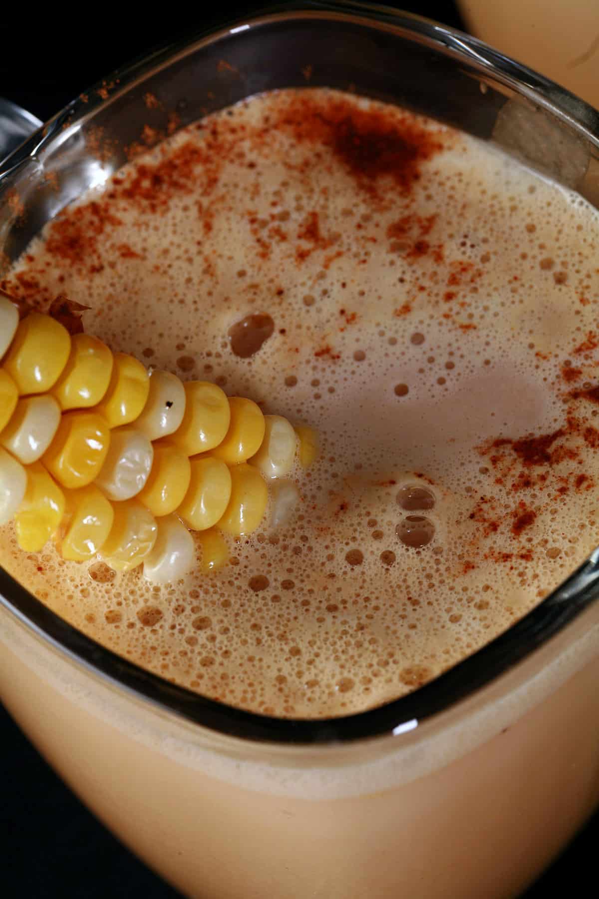 A close up photo of a glass mug of corn cappuccino.
