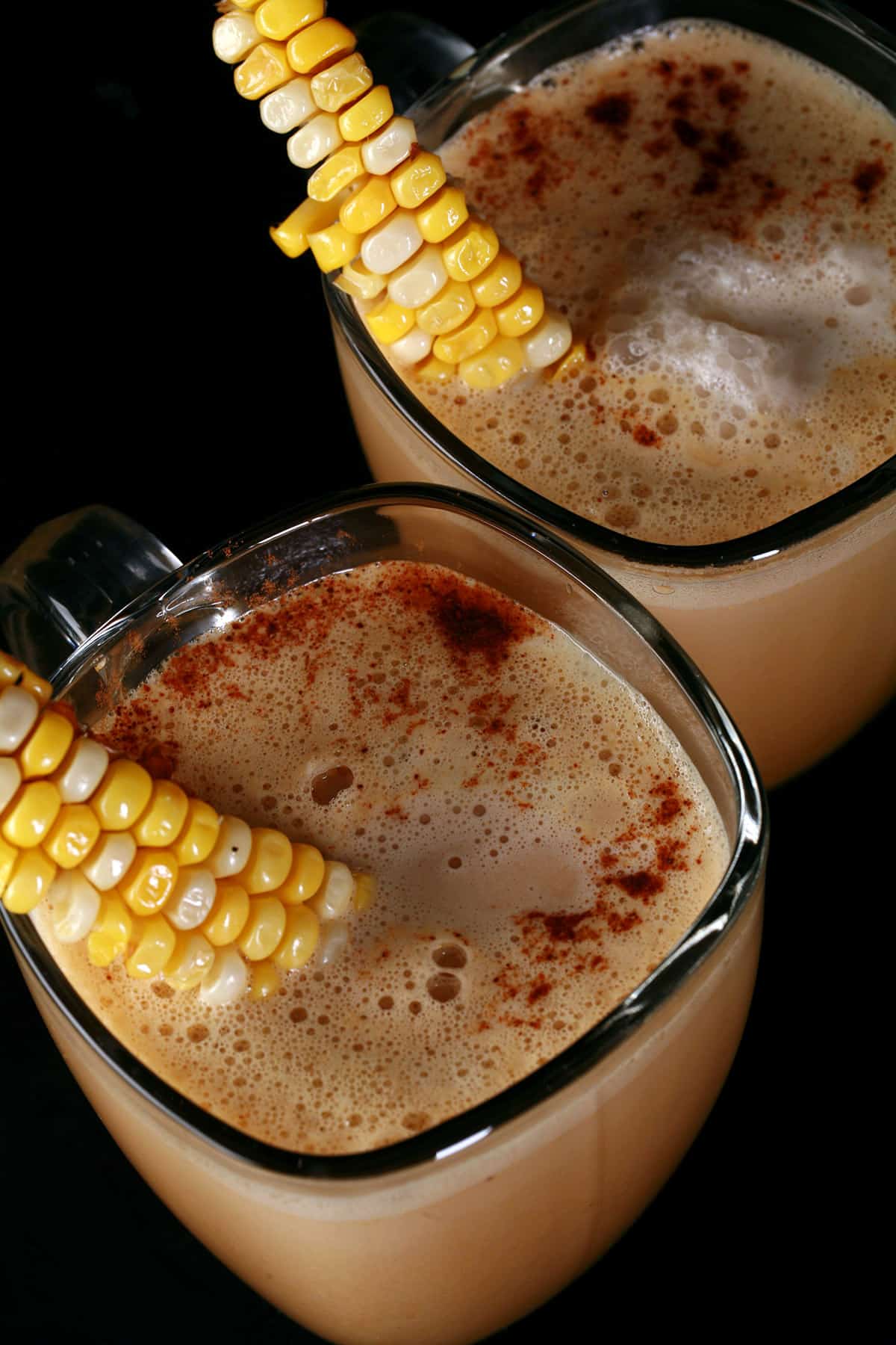 2 glass mugs of con cappuccino, garnished with narrow lengths of corn on the cob.