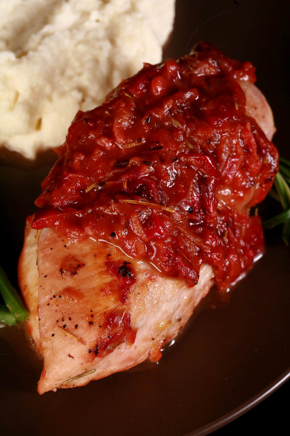 A serving of cranberry chicken on a plate with green beans and mashed cauliflower.