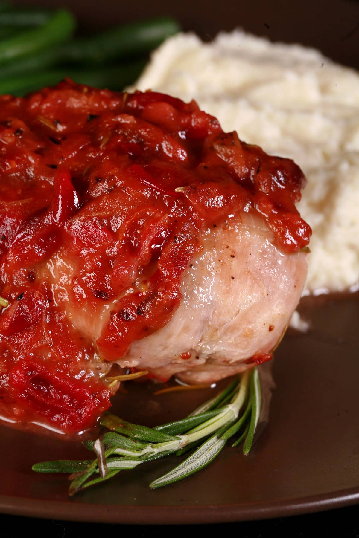 A serving of cranberry chicken on a plate with green beans and mashed cauliflower.