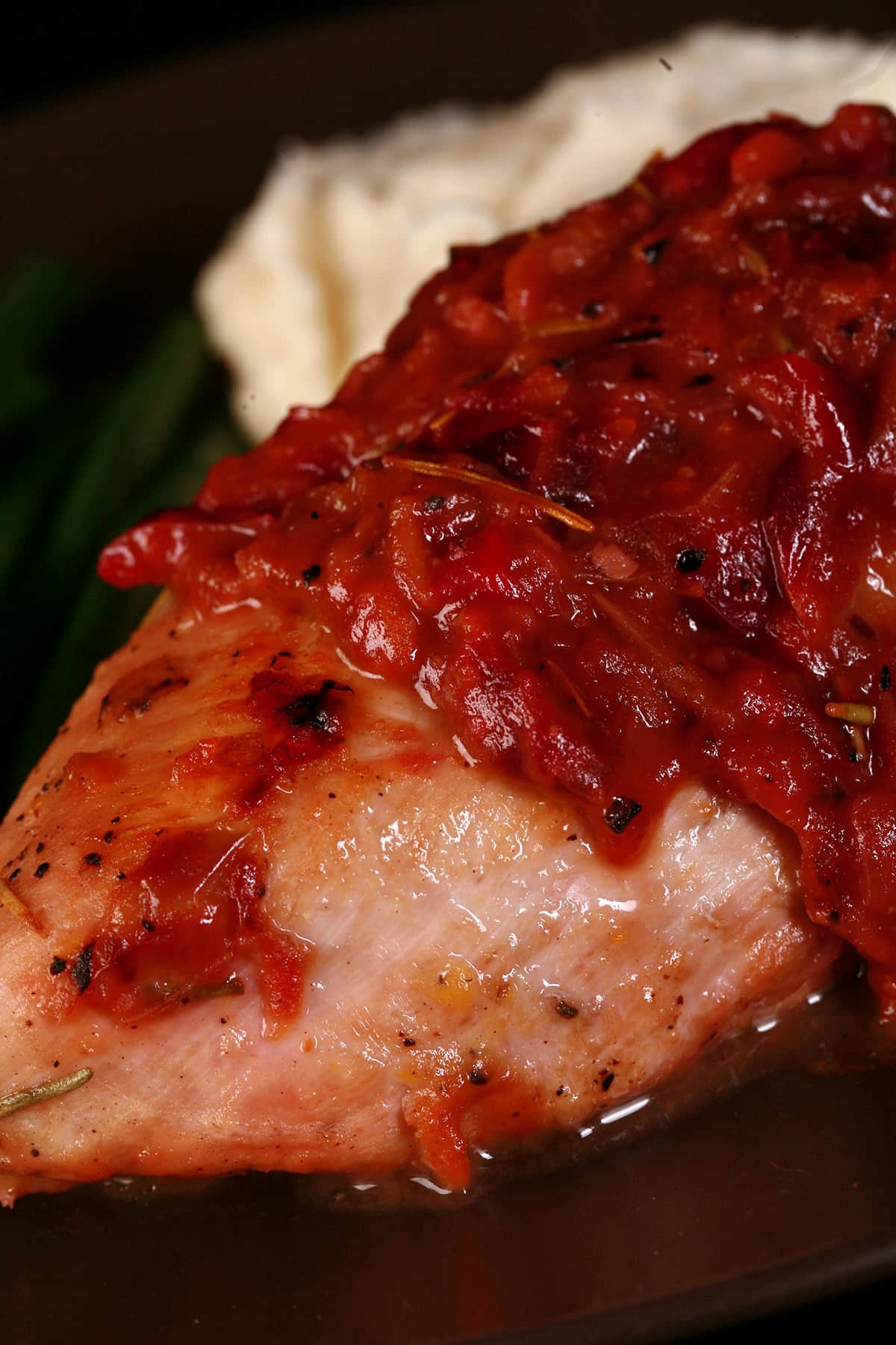 A serving of cranberry chicken on a plate with green beans and mashed cauliflower.