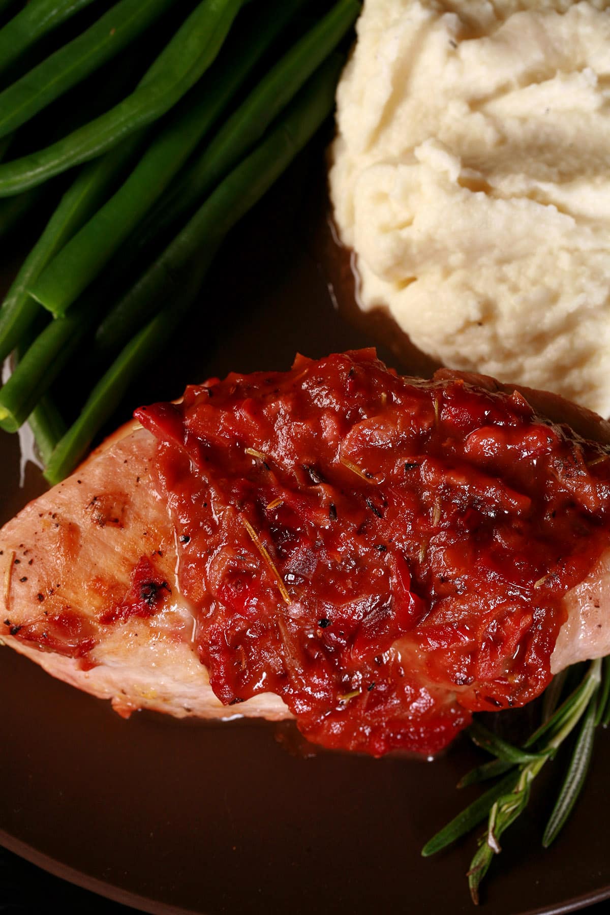 A serving of cranberry chicken on a plate with green beans and mashed cauliflower.