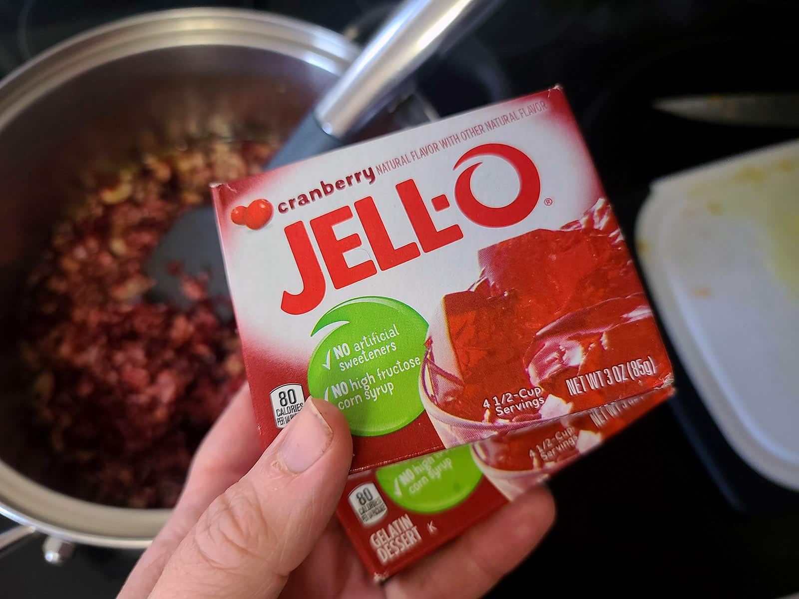 A hand holding a box of cranberry Jello.