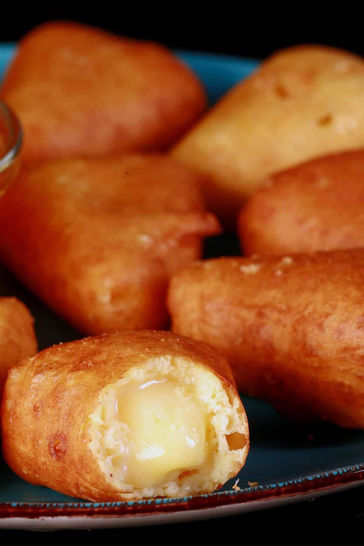 A plate of battered gluten free deep fried brie cheese wedges, around a bowl of apricot preserves. One has a bite, with brie oozing out.