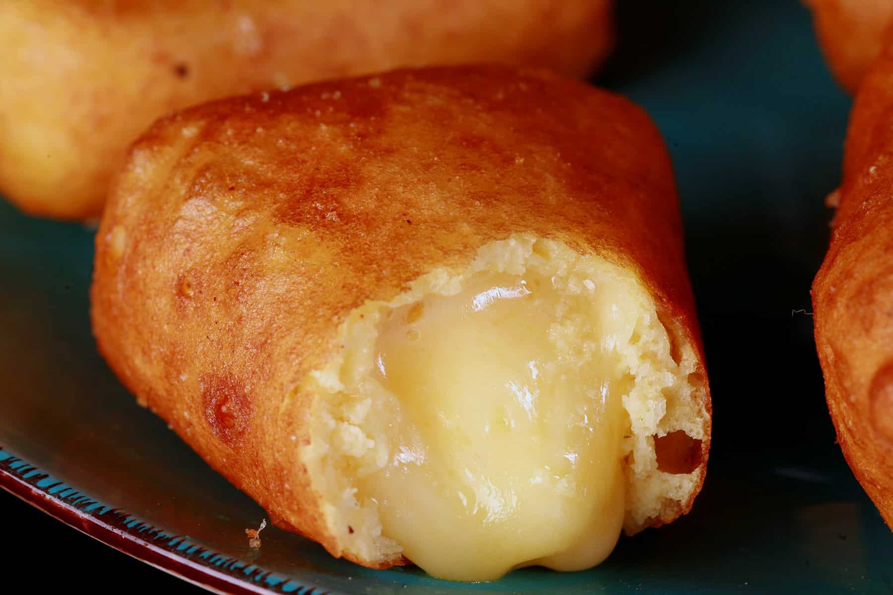 A plate of battered gluten free deep fried brie cheese wedges, around a bowl of apricot preserves. One has a bite, with brie oozing out.