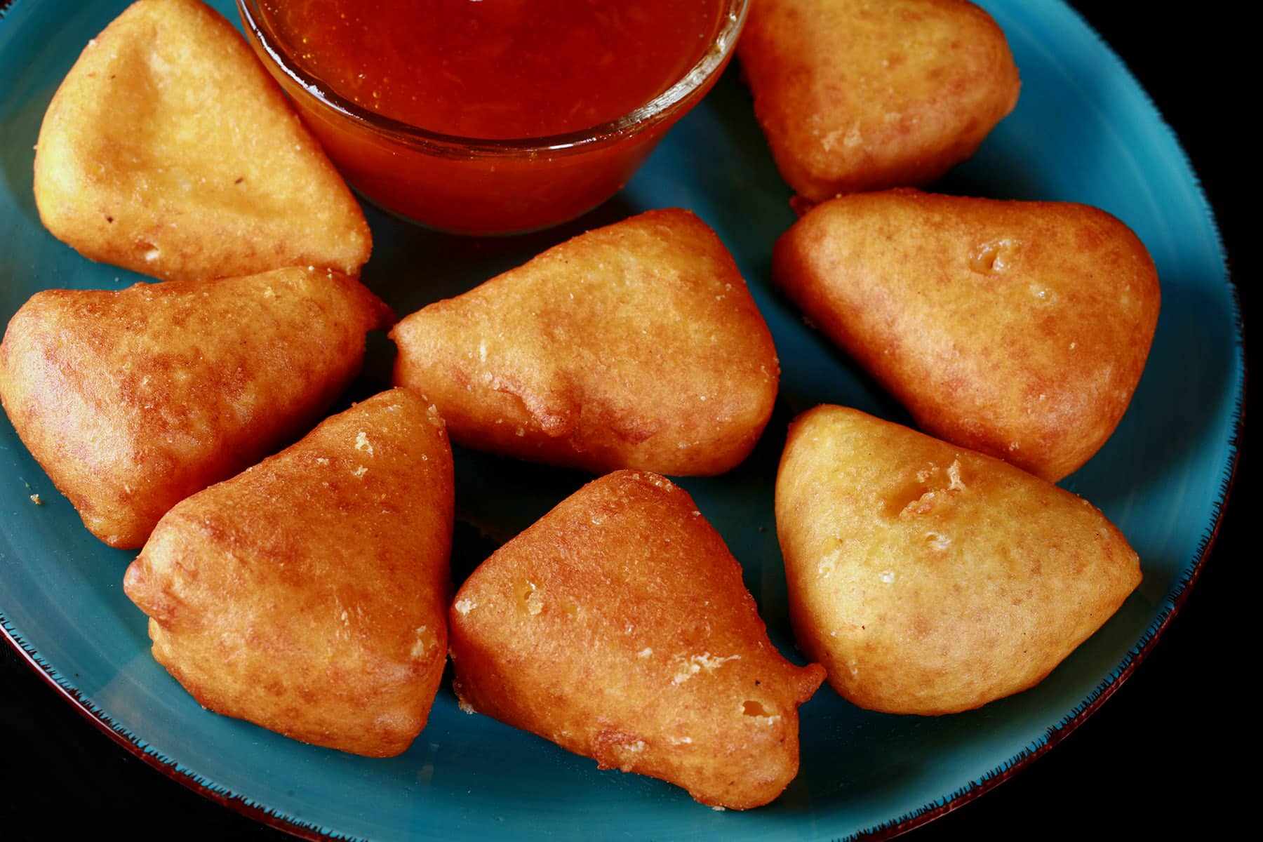 A plate of battered, deep fried brie cheese wedges, around a bowl of apricot preserves.