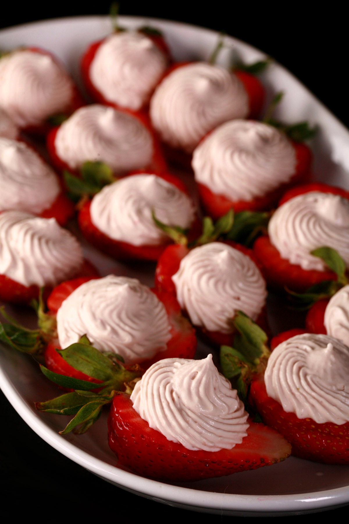 A white plate with deviled strawberries, filled with a cream cheese and balsamic vinegar whipped cream.