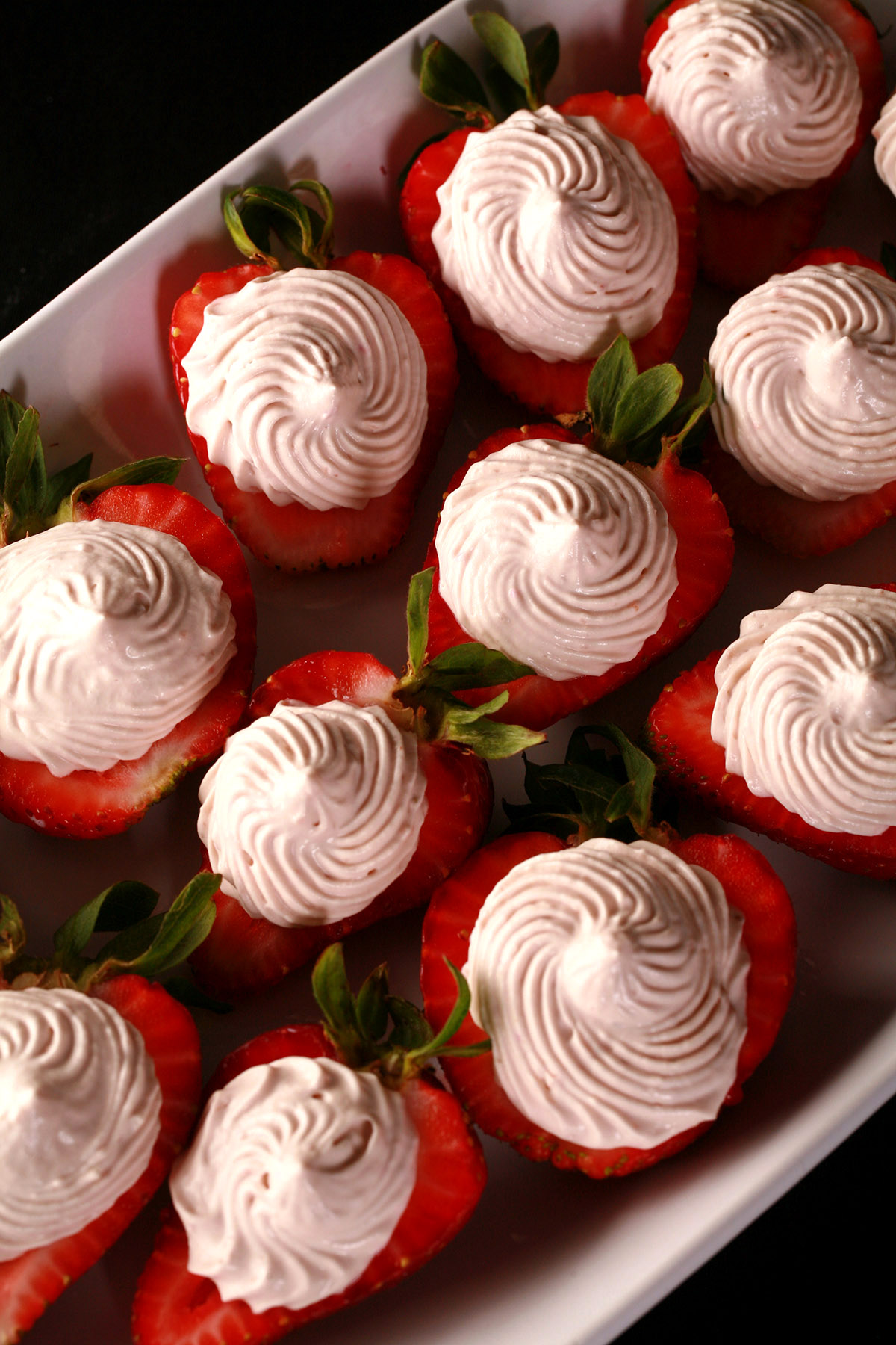 A white plate with deviled strawberries, filled with a cream cheese and balsamic vinegar whipped cream.