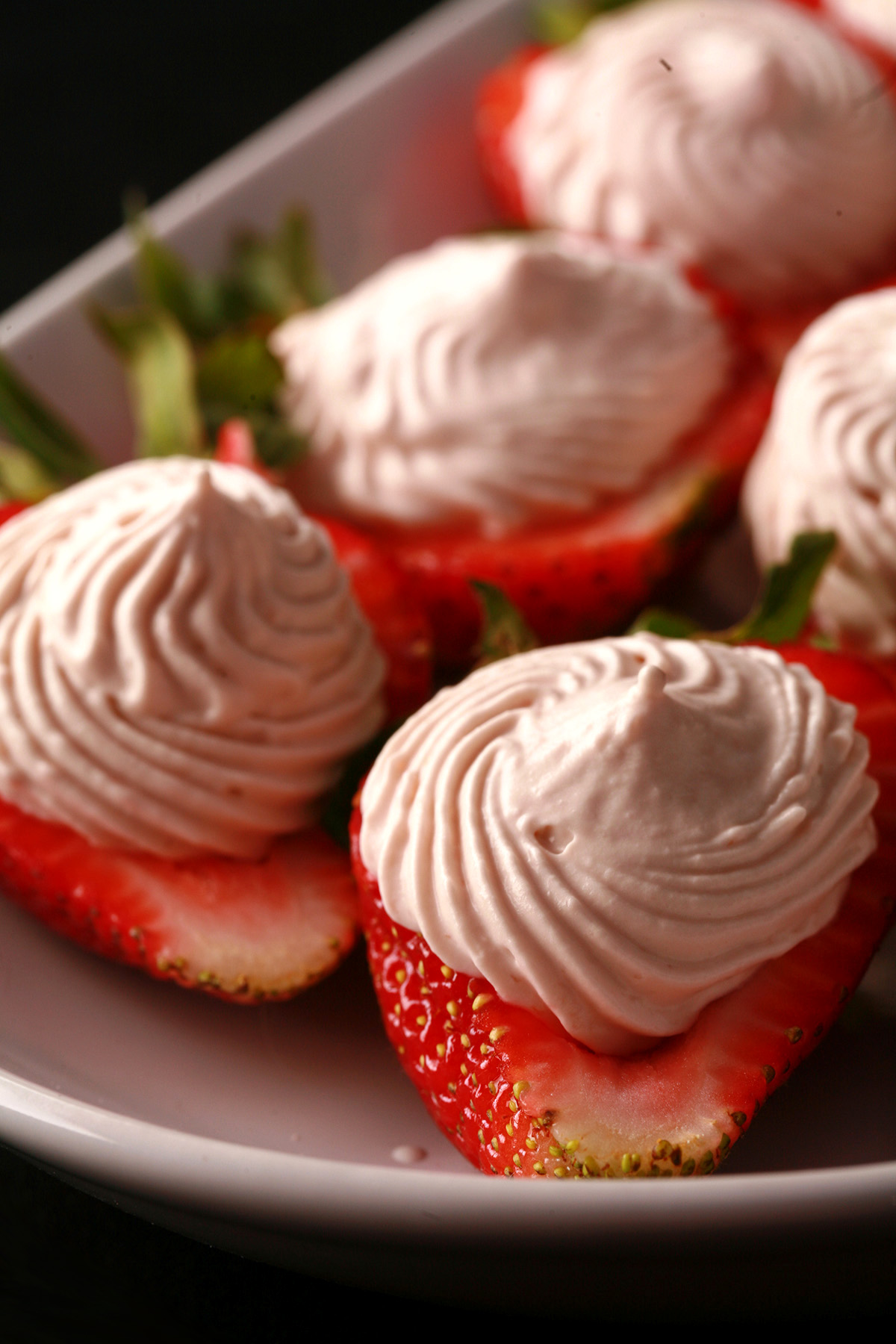 A white plate with deviled strawberries, filled with a cream cheese and balsamic vinegar whipped cream.