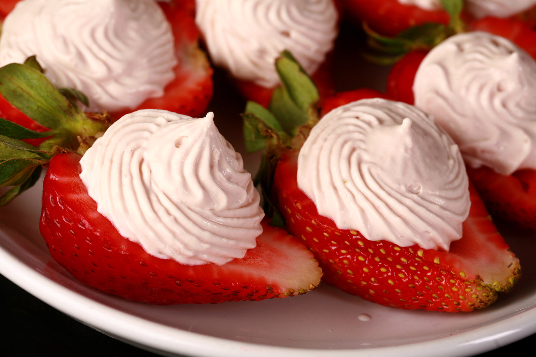 A white plate with deviled strawberries, filled with a cream cheese and balsamic vinegar whipped cream.