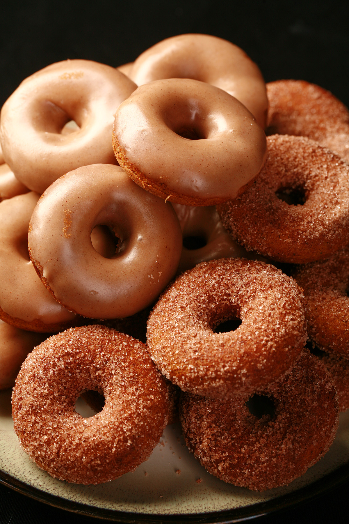 Close up view of gluten-free pumpkin spice mini doughnuts. Some are coated in cinnamon sugar, others are glazed with a tan coloured frosting.