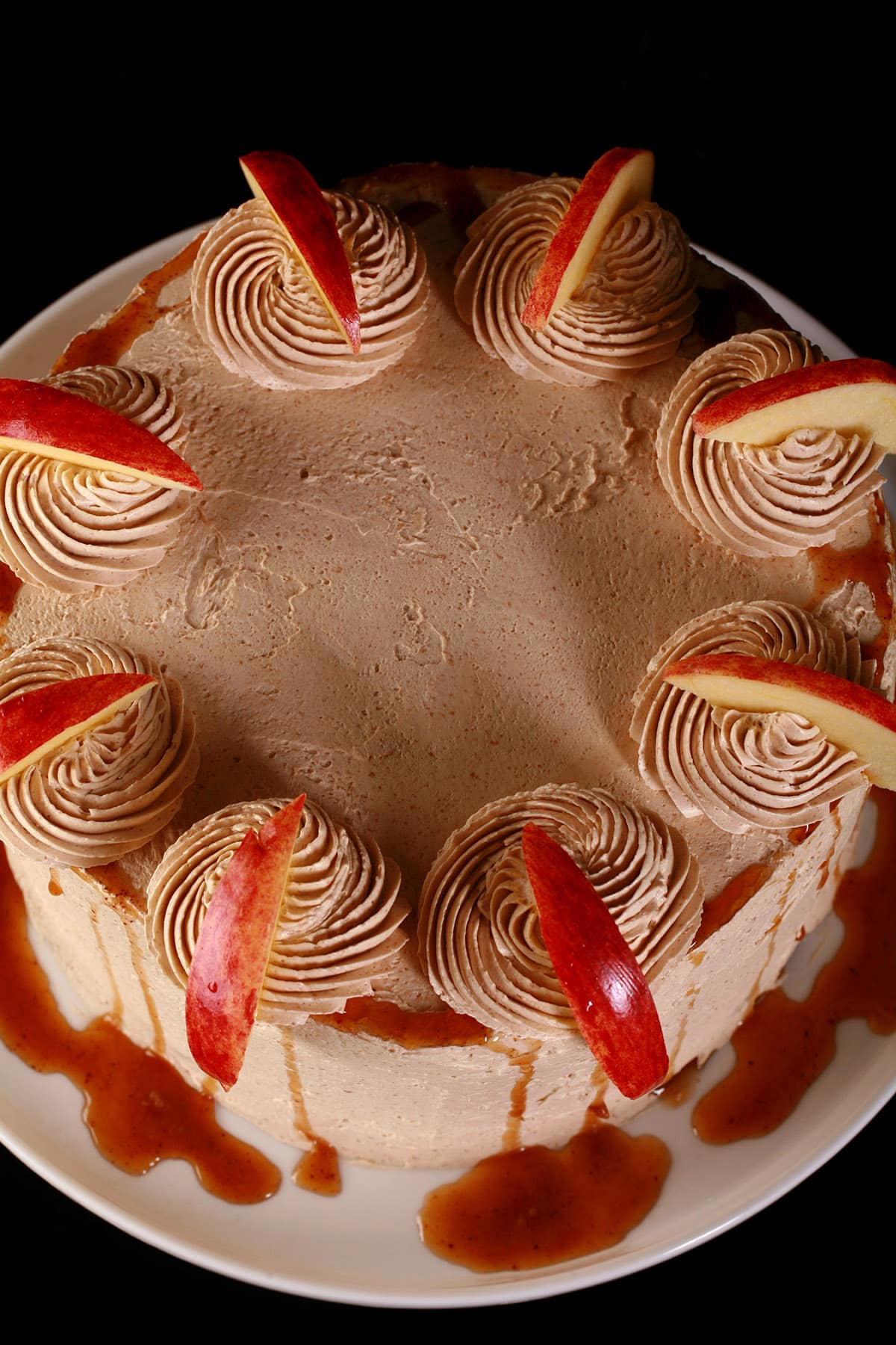 A round gluten-free apple cake, garnished with syrup and apple slices.