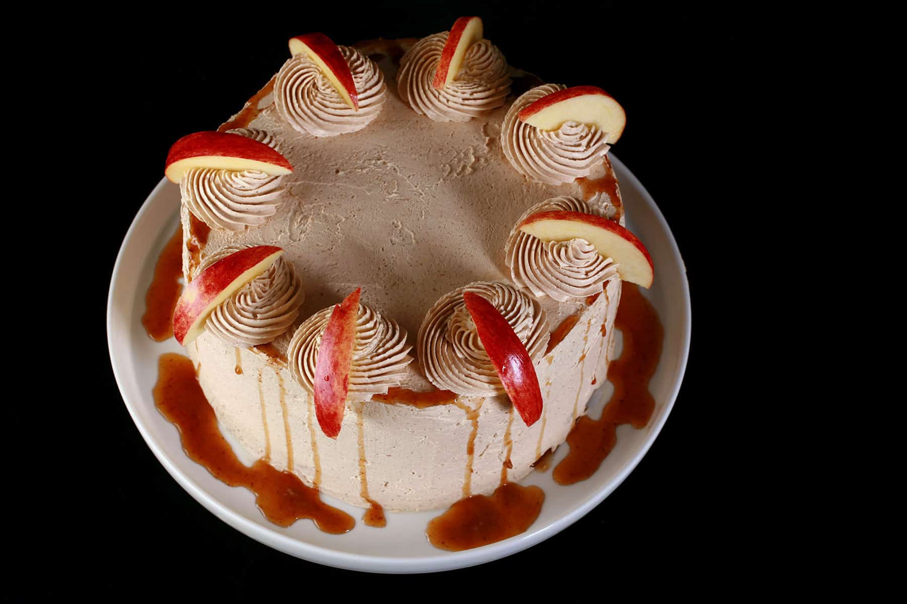 A round gluten-free apple cake, garnished with syrup and apple slices.