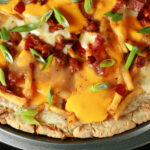 A close up view of a gluten-free poutine pizza - A pizza crust topped with gravy, fries, cheese curds, chredded cheese, bacon, and green onions!