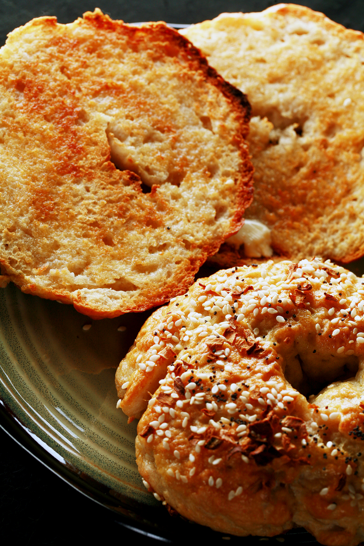 A close up view of two toasted gluten-free bagels on a plate. One is coated with everything seasoning.