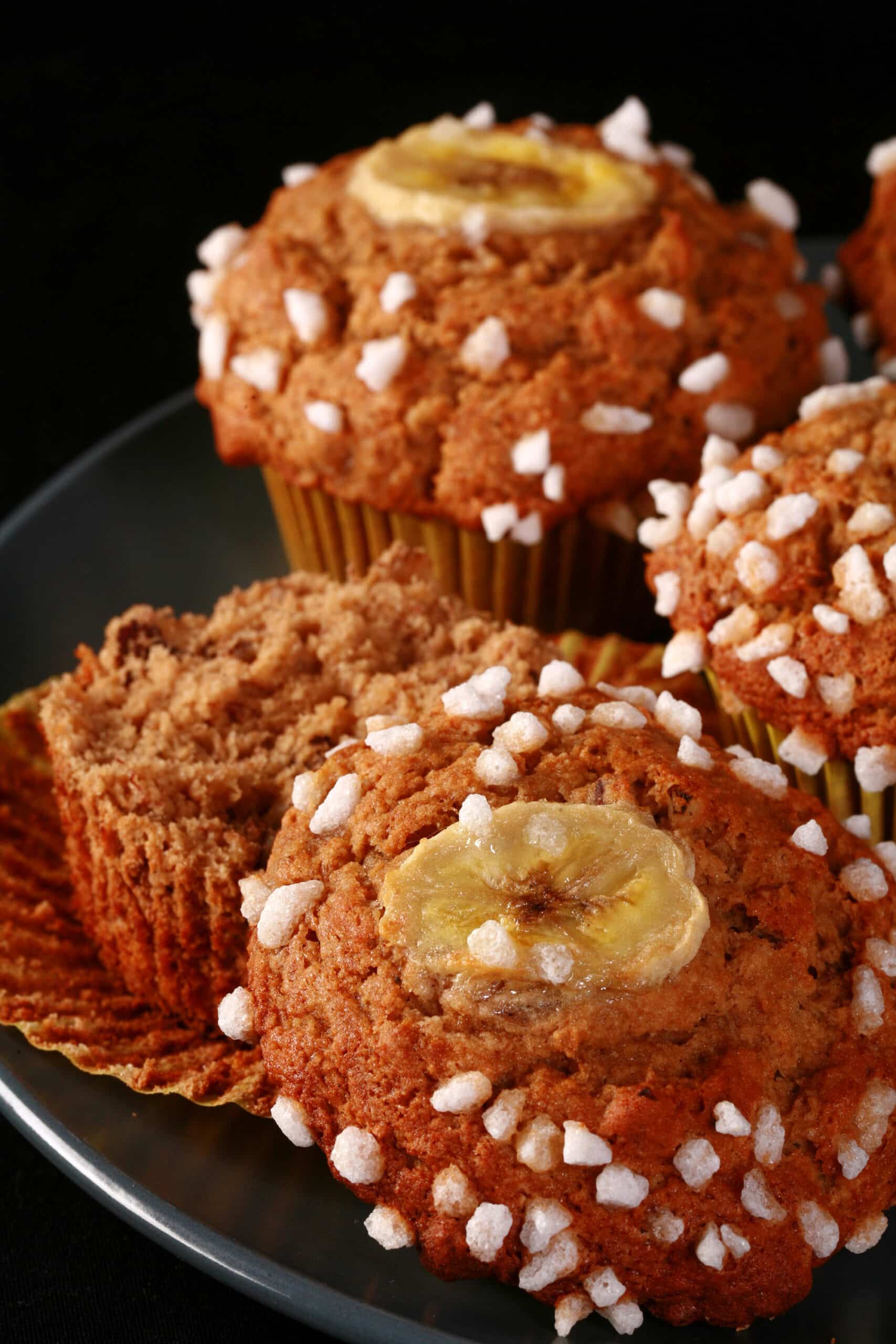 A plate of gluten-free banana muffins, topped with coarse sugar and banana slices.