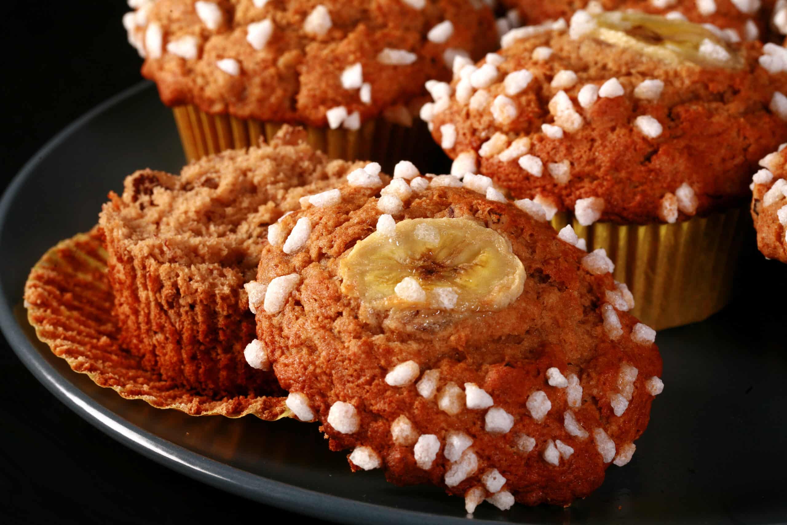 A plate of gluten free banana muffins, topped with coarse sugar and banana slices.