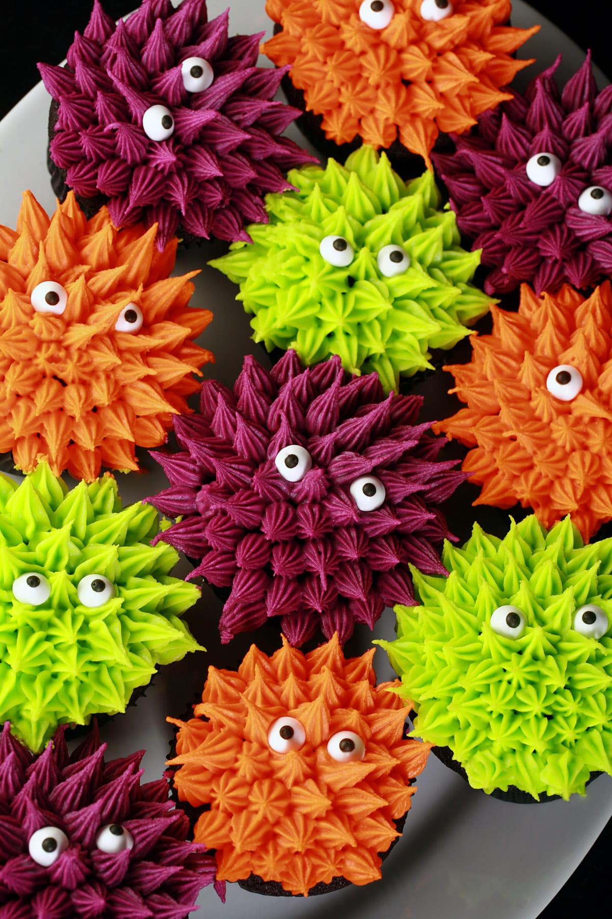 A plate full of gluten free black velvet cupcakes, decorated to look like brightly coloured Halloween monsters.