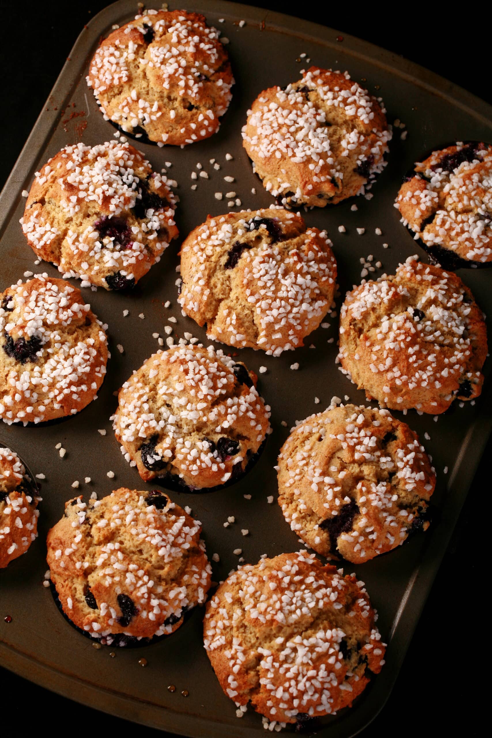 Several sugar topped gluten free blueberry muffins in a muffin pan.