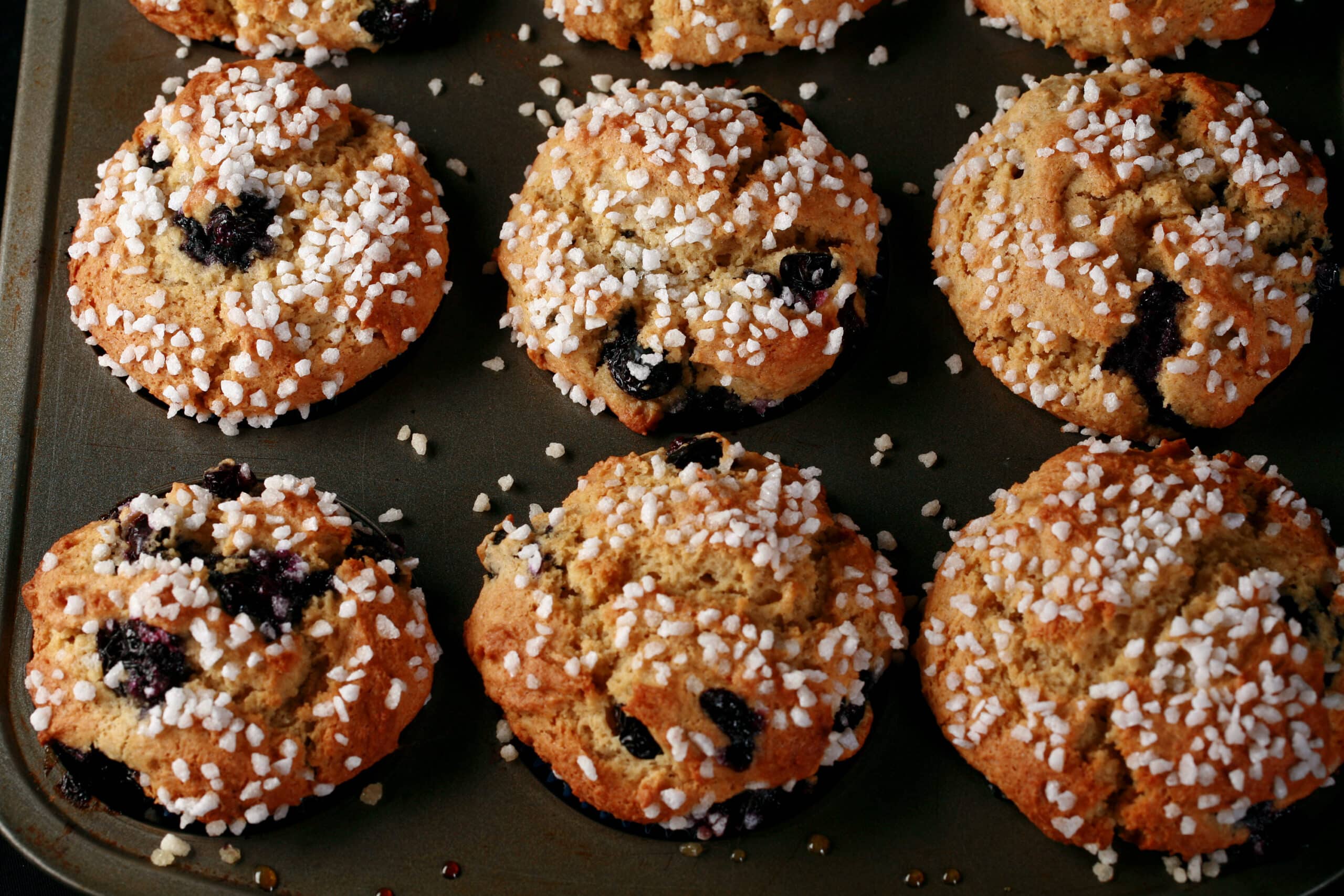 Several sugar topped gluten-free blueberry muffins in a muffin pan.