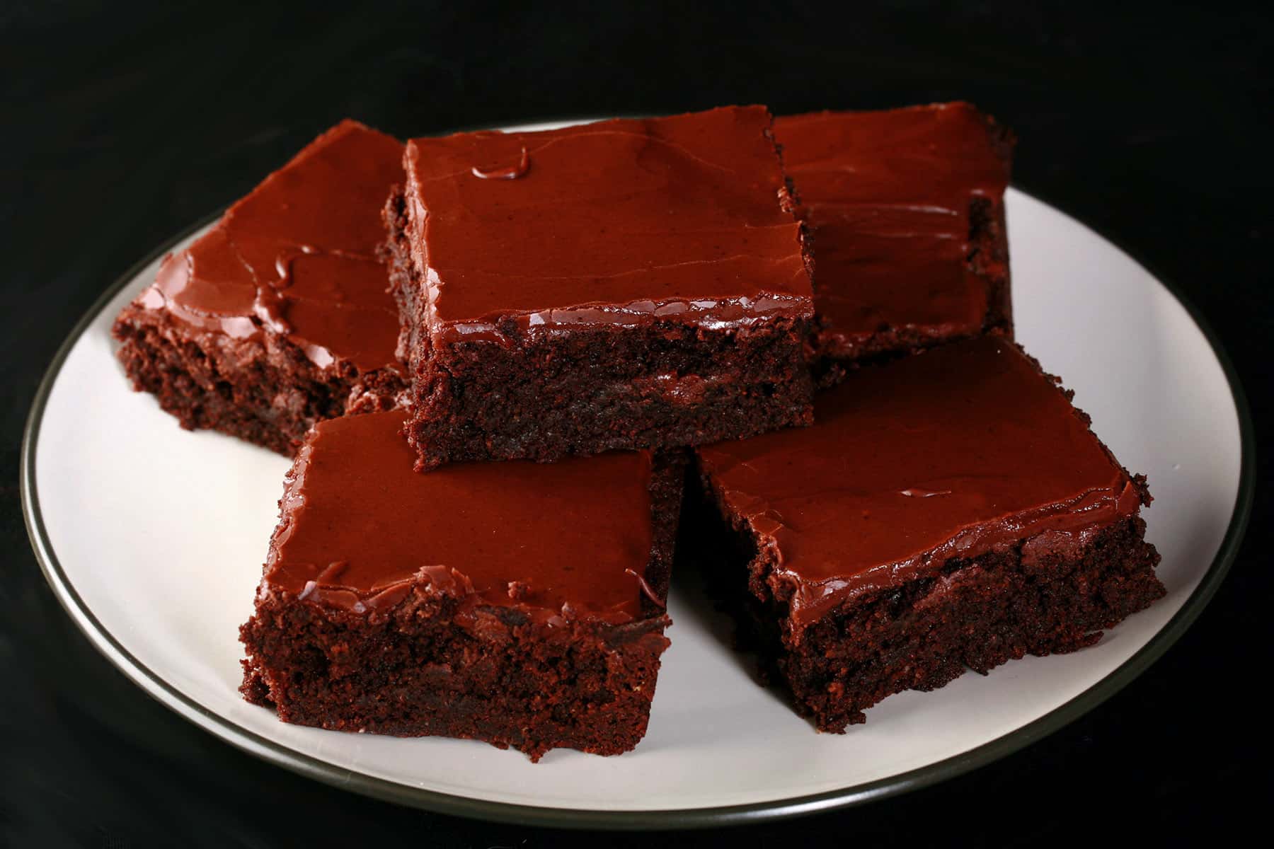 A plate of gluten free brownies with chocolate frosting.