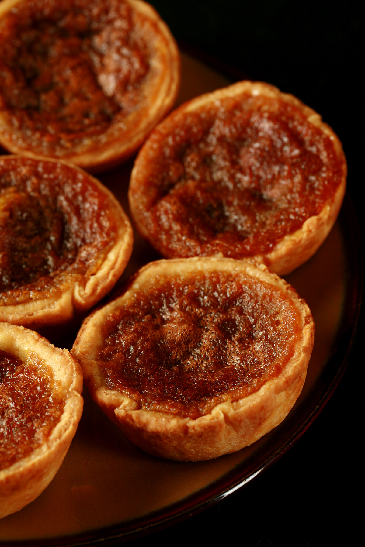 A brown plate is crowded with gluten-free buttertarts - mini tarts with a gooey sugar filling and raisins