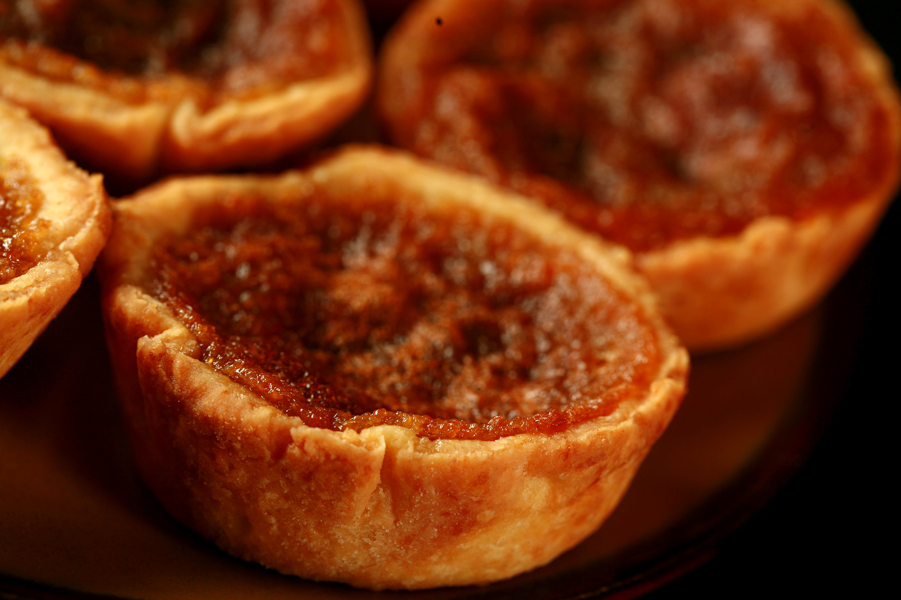 A brown plate is crowded with gluten-free butter tarts - mini tarts with a gooey sugar filling and raisins