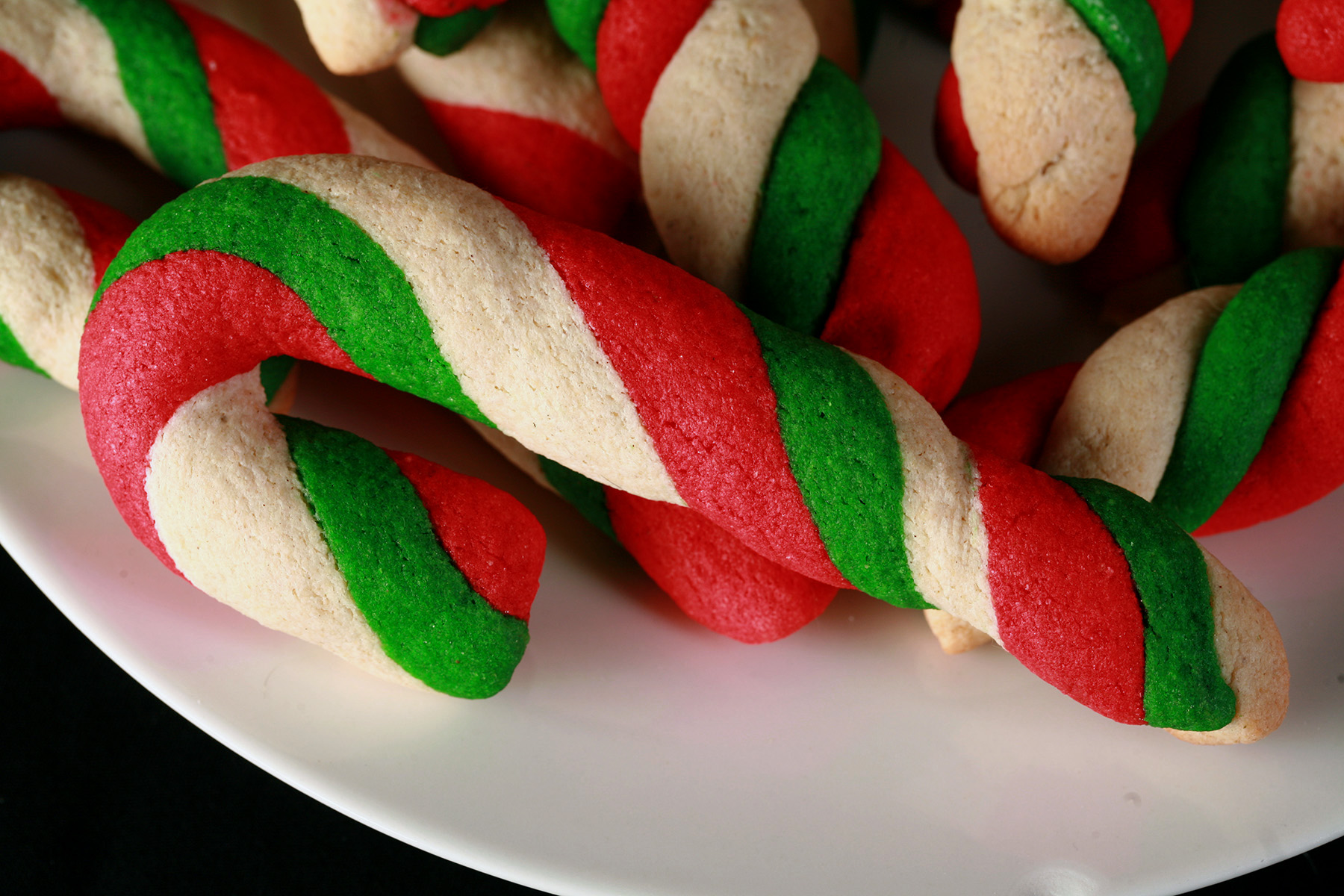 Gluten-Free Candy Cane cookies - candy cane shaped cookies, made from lengths of red, green, and white twisted dough - on a plate.