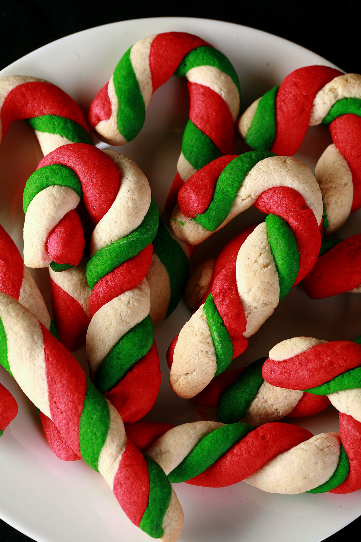 Gluten-Free Candy Cane cookies - candy cane shaped cookies, made from lengths of red, green, and white twisted dough - on a plate.