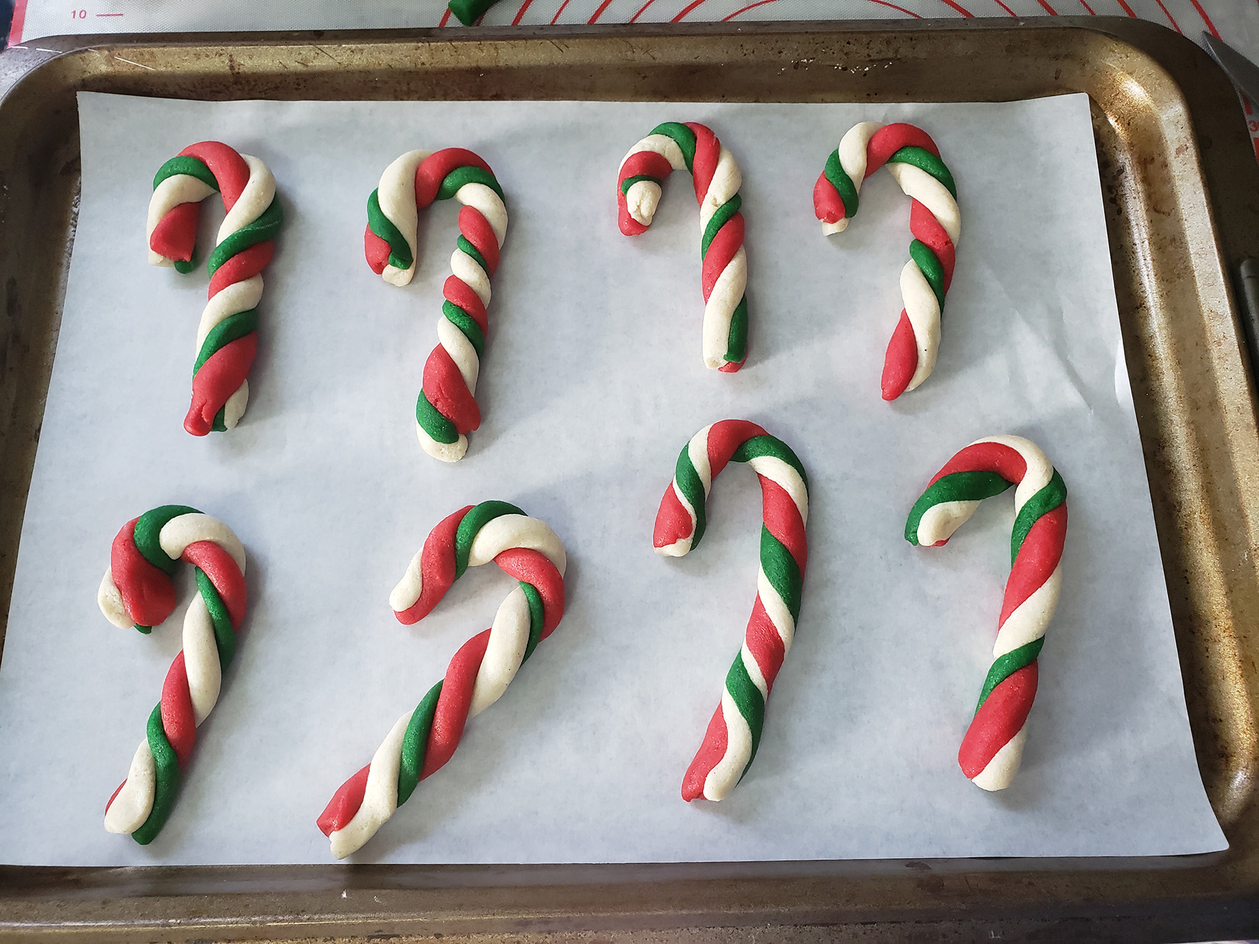Candy cane shaped cookies made of red, white, and green dough are arranged on a parchment paper lined baking sheet.