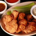 A plate of deep fried gluten-free chicken nuggets, celery, and dip.