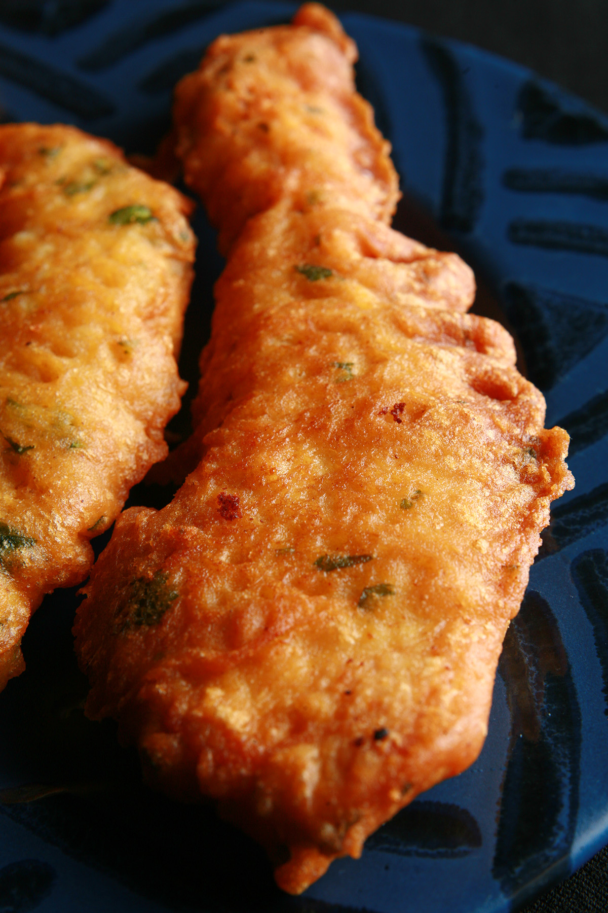 Several strips of gluten-free chicken pakora on a blue plate. They are golden deep fried, with flecks of green cilantro.