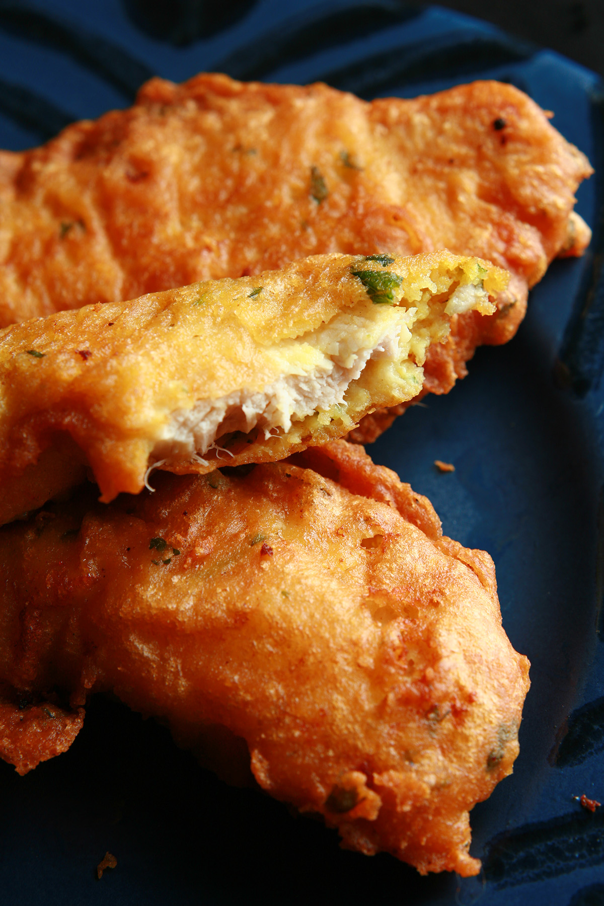 Several strips of gluten-free chicken pakora on a blue plate. They are golden deep fried, with flecks of green cilantro.