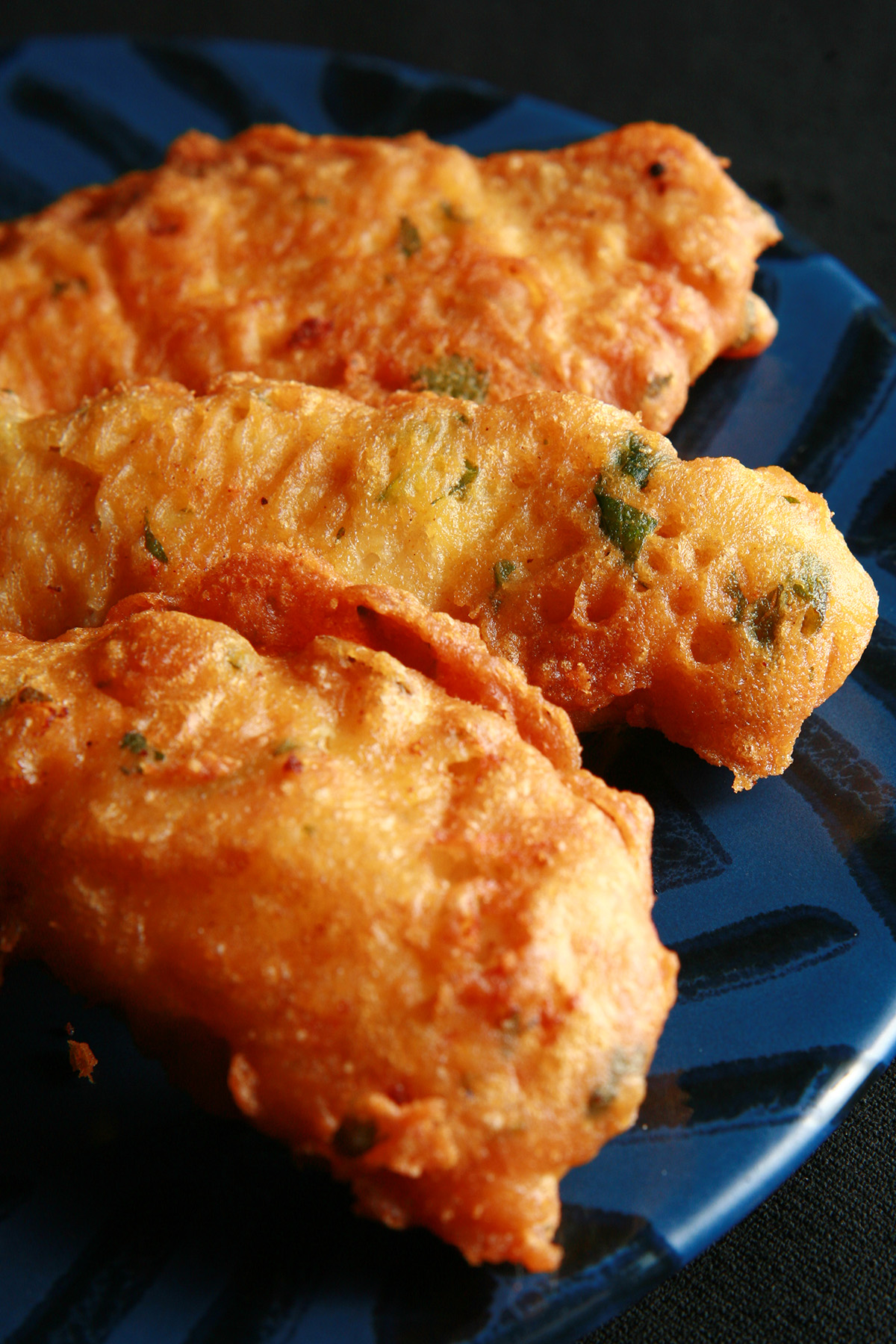 Several strips of gluten-free chicken pakora on a blue plate. They are golden deep fried, with flecks of green cilantro.
