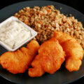 Gluten-Free Cod Cheeks and Dressing, on a round, blue plate. There is a small dish of tartar sauce on the plate, as well.