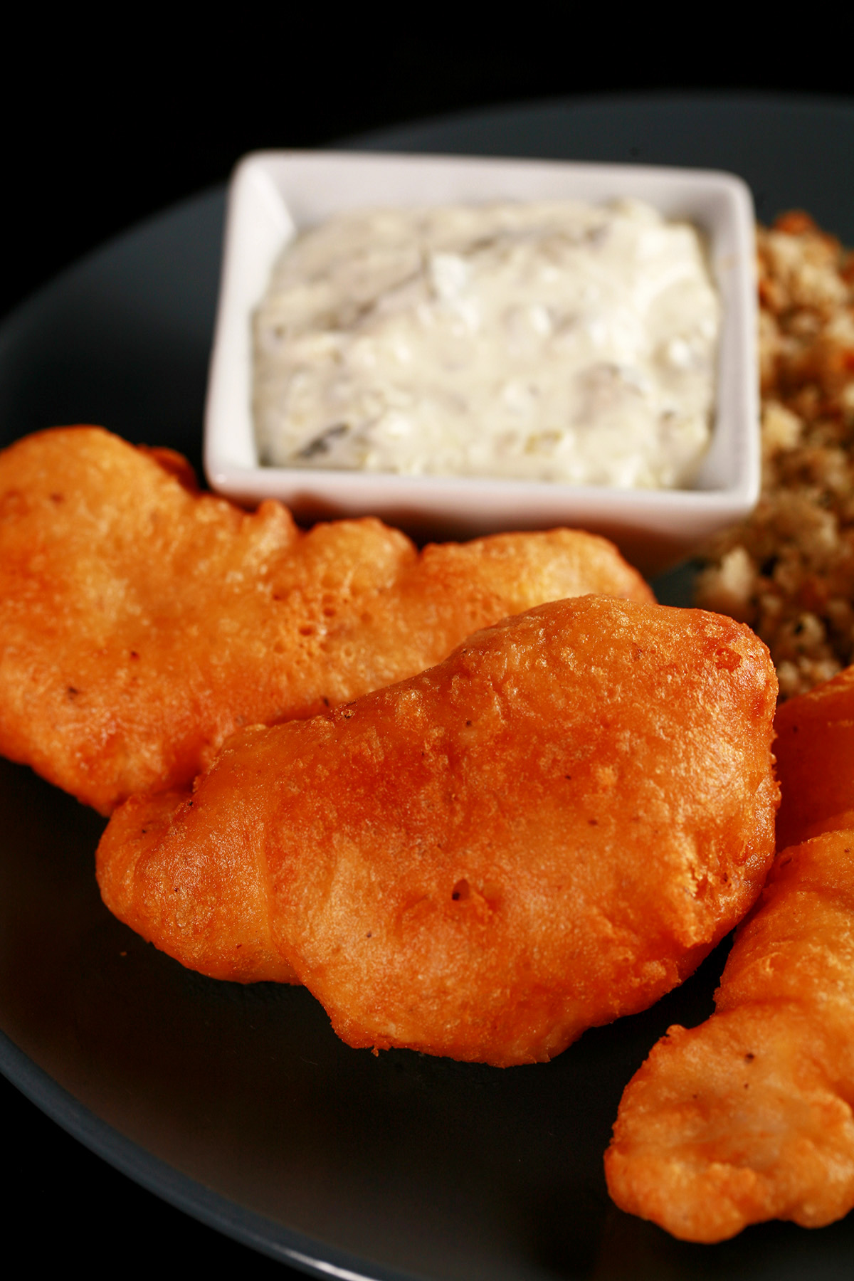 Gluten-Free Cod Cheeks a on a round, blue plate. There is a small dish of tartar sauce on the plate, as well.